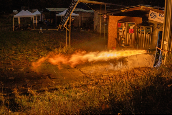 rocket firing on a test stand, bright flames emerging from the engine horizontally