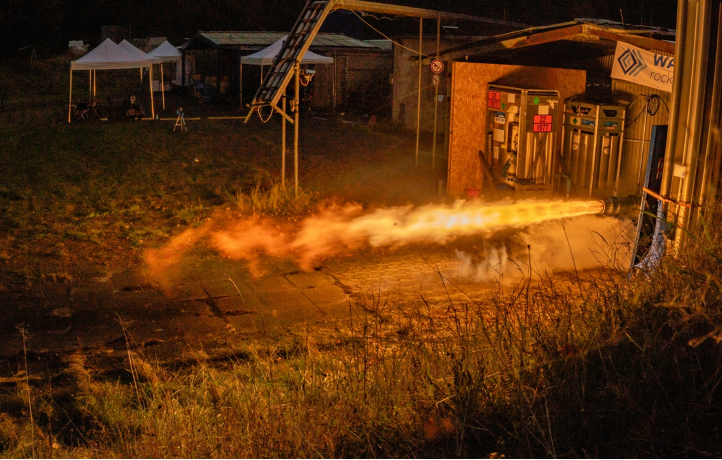 rocket firing on a test stand, bright flames emerging from the engine horizontally